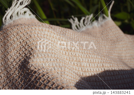 Woven beige blanket with fringe lying on green grass outdoors Woven beige blanket with fringe lying on green grass outdoors 143883241