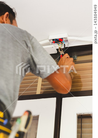 Electrician using pliers to work on electrical wiring inside an open wall mounted junction box. Electrician using pliers to work on electrical wiring inside an open wall mounted junction box. 143884949
