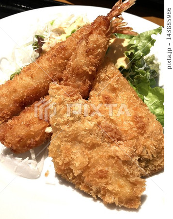 皿に盛り付けられたサクサクのエビフライと白身魚フライの盛り合わせ 皿に盛り付けられたサクサクのエビフライと白身魚フライの盛り合わせ 143885986