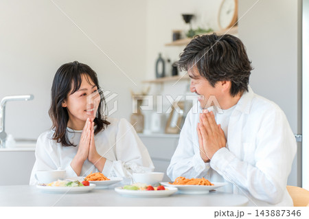 家の食卓で手を合わせていただきますをする笑顔の夫婦。 家の食卓で手を合わせていただきますをする笑顔の夫婦。 143887346
