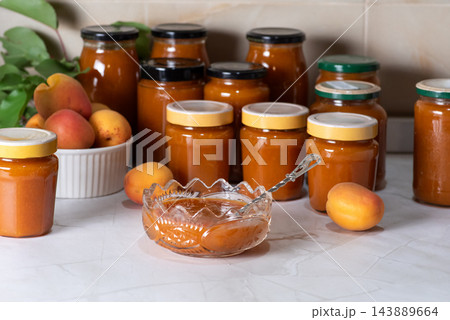 Homemade apricot jam jars arranged on kitchen counter with fresh fruit 143889664