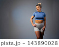 Fit young woman in blue crop top and gray leggings standing confidently in studio 143890028