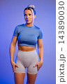 Fit young woman in blue crop top and gray leggings posing confidently against purple background 143890030
