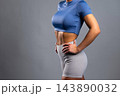 Fit woman in blue crop top and gray leggings showing toned abs with hands on hips 143890032