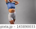Fit woman in blue crop top and gray athletic shorts posing confidently against gray background 143890033