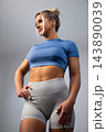 Fit young woman in blue crop top and gray leggings posing confidently in studio 143890039