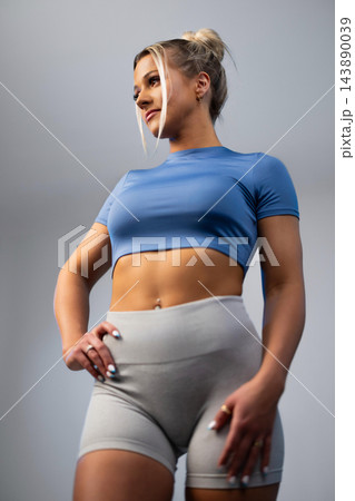 Fit young woman in blue crop top and gray leggings posing confidently in studio 143890039
