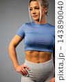 Fit young woman in blue crop top and gray leggings posing confidently with hand on hip 143890040