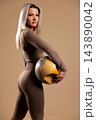 Fit woman in brown workout outfit holding yellow medicine ball in studio setting 143890042