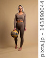 Fit woman in brown workout outfit holding medicine ball in studio setting 143890044
