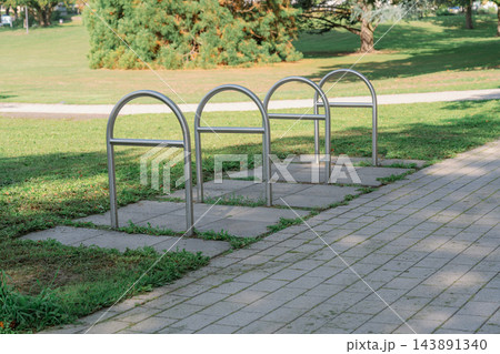 Outdoor stainless steel bike stands located in a quiet green park along a paved footpath under bright sunlight, representing cycling infrastructure 143891340