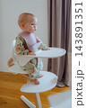 Minimalist shot of a sweet infant sitting in an ergonomic high chair against linen curtains, showcasing modern nursery furniture and baby routine 143891351