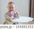 Close-up of a cheerful infant with hands on table laughing directly at camera, capturing genuine emotions, positive childhood, and baby health 143891353