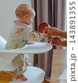 Minimalist scene of a cute toddler girl in a designer high chair reaching for food bowl with father caring for her in a cozy home environmen 143891355