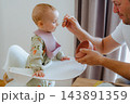 Close-up of a dad holding a silicone bowl and spoon to feed his little child in a bright home kitchen setting, highlighting parent care and child nutrition 143891359