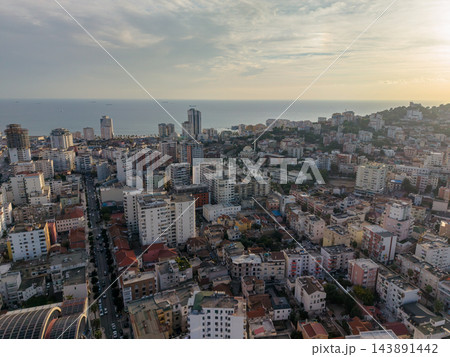 Durres Albania appears in broad coastal panorama at sunset, with dense urban buildings beside Adriatic Sea. Tall towers, wooded hillside and distant ships distinguish this seaside city view. Durres Albania appears in broad coastal panorama at sunset, with dense urban buildings beside Adriatic Sea. Tall towers, wooded hillside and distant ships distinguish this seaside city view. 143891442