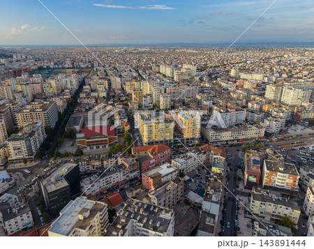 Durres Albania spreads across dense coastal cityscape, with apartment blocks and streets filling foreground. Aerial view reveals Adriatic shoreline and distant hills beneath broad blue sky. 143891444