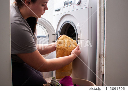 Woman loads pile of dirty clothes into modern washing machine, using home appliances to simplify laundry. Automated washing makes household routines more convenient and efficient Woman loads pile of dirty clothes into modern washing machine, using home appliances to simplify laundry. Automated washing makes household routines more convenient and efficient 143891706