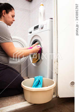 Woman puts dirty clothes into washing machine as part of managing everyday life. Regular laundry routine helps organize household responsibilities and keep daily home tasks under control Woman puts dirty clothes into washing machine as part of managing everyday life. Regular laundry routine helps organize household responsibilities and keep daily home tasks under control 143891707