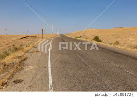 Empty asphalt road and utility poles crossing dry arid landscape in southern Tajikistan Empty asphalt road and utility poles crossing dry arid landscape in southern Tajikistan 143891727