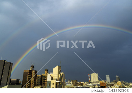 雨上がりの夕空、都市のビル群を大きく包み込む綺麗な虹 143892508