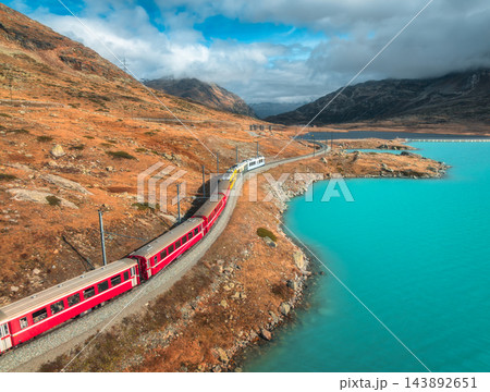 Aerial view of red train near alpine mountain lake and cloudy sky 143892651