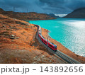 Aerial view of red train near alpine mountain lake and cloudy sky 143892656