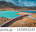 Aerial view of red train near alpine mountain lake and cloudy sky 143893245