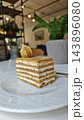 Layered vanilla cream cake slice with golden sponge, textured topping, and dried fruit garnish on a white ceramic plate in a softly lit restaurant interior 143896080