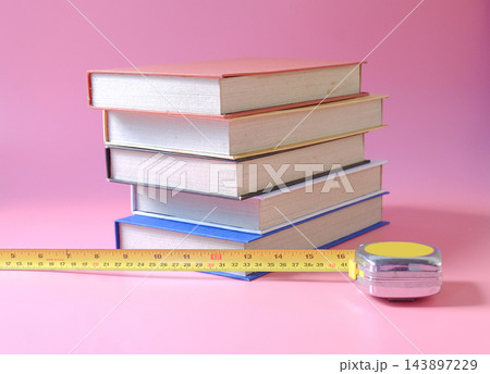 A stacks of hard cover books with measuring tape on background. A stacks of hard cover books with measuring tape on background. 143897229