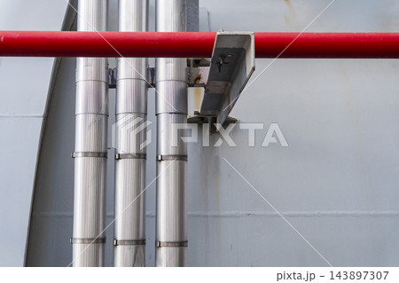 Vertical insulated metal pipes and a horizontal red safety pipeline mounted on an industrial wall. 143897307