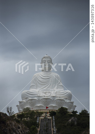 Massive white seated Buddha statue on a lotus pedestal at Linh Phong Temple in Quy Nhon Vietnam rising above a hillside stairway under a dramatic overcast sky in a powerful religious landmark shot. Massive white seated Buddha statue on a lotus pedestal at Linh Phong Temple in Quy Nhon Vietnam rising above a hillside stairway under a dramatic overcast sky in a powerful religious landmark shot. 143897316