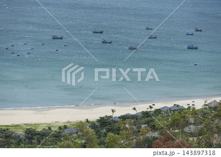 Scenic view of traditional fishing boats floating on turquoise sea along a sandy beach in Quy Nhon, Vietnam. Scenic view of traditional fishing boats floating on turquoise sea along a sandy beach in Quy Nhon, Vietnam. 143897318