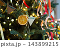 Dried orange slice ornament hanging on Christmas tree with colorful ribbons and warm lights bokeh 143899215