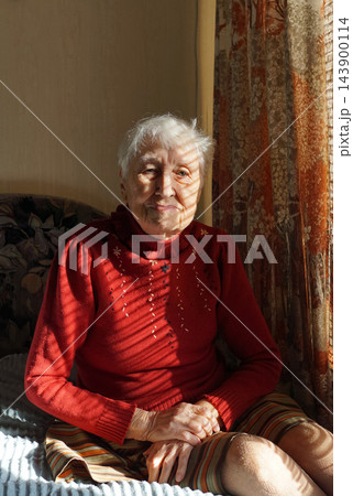 Old lonely woman sitting near the window in his house. Old lonely woman sitting near the window in his house. 143900114