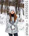 Young girl in silver winter coat holding snow in hands during a snowy forest walk 143900201