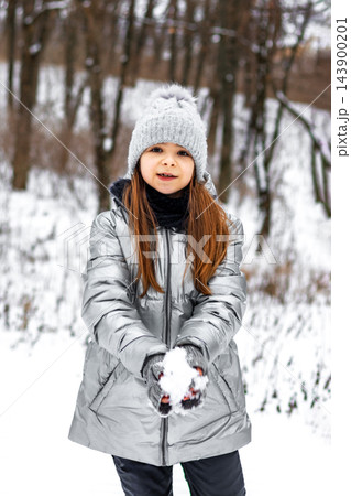 Young girl in silver winter coat holding snow in hands during a snowy forest walk Young girl in silver winter coat holding snow in hands during a snowy forest walk 143900201