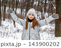 Young girl in gray winter coat and knit hat enjoying snow in a snowy forest 143900202