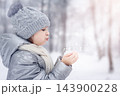 A young girl blows on snow in her hands and snowflakes fly away against the backdrop of a winter park. 143900228