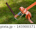 Ratchet strap secures cargo equipment to a metal stake on a grassy lawn 143900371