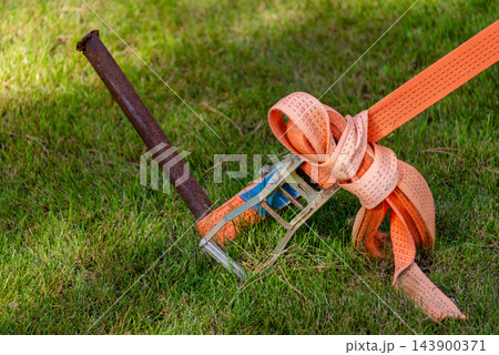 Ratchet strap secures cargo equipment to a metal stake on a grassy lawn 143900371