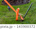 Ratchet strap secures cargo equipment to a metal stake on a grassy lawn 143900372