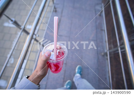 Hand holding a transparent plastic cup of cold pink bubble tea or berry milkshake with black tapioca pearls and a straw Hand holding a transparent plastic cup of cold pink bubble tea or berry milkshake with black tapioca pearls and a straw 143900590