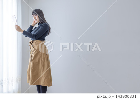 窓辺で手鏡を見ながら髪を整える若い女性 窓辺で手鏡を見ながら髪を整える若い女性 143900831