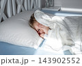 Sleeping child resting on bed with head on pillow, bathed in soft morning sunlight inside calm bedroom. Concept of peaceful sleep, comfort, safety, family care, wellbeing, minimal interior mood 143902552