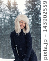 Portrait young adult mid age smile woman enjoy have fun walking in park forest snowfall cold winter day. Female portrait person happiness wear black ski overall stylish fur hat snowflakes background 143902559
