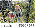 Cute little funny caucasian blond kid boy enjoy having fun walk metal net tunnel playground in treetop adventure amusement park Saarland. Children outdoors nature extreme sport activities concept 143902563