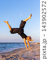 Active child performing handstand acrobatics on sandy beach during golden hour, showing balance, strength, flexibility, playful summer energy. Sea waves sunset light outdoor childhood fitness freedom 143902572