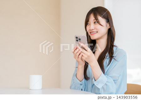 スマホで嬉しい知らせを受け取り笑顔を見せる20代の若い女性。 スマホで嬉しい知らせを受け取り笑顔を見せる20代の若い女性。 143903556