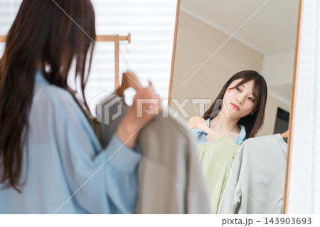 鏡の前で洋服を比較しながらコーディネートに悩む若い女性。 鏡の前で洋服を比較しながらコーディネートに悩む若い女性。 143903693